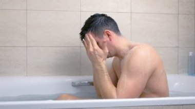 Adam küvette otururken yıkanıyor ve masaj hareketleri ile yüzüne scrub uygulayarak.