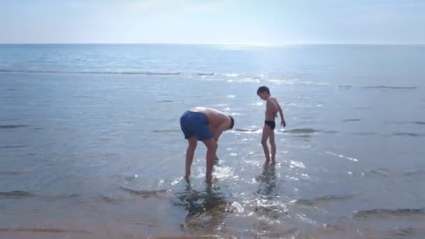 Vater und Sohn starten das Spielzeugmotorboot am Meeresstrand. — Stockvideo
