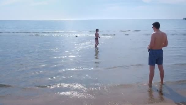 Папа и сын запускают игрушечную моторную лодку на морском пляже. . — стоковое видео