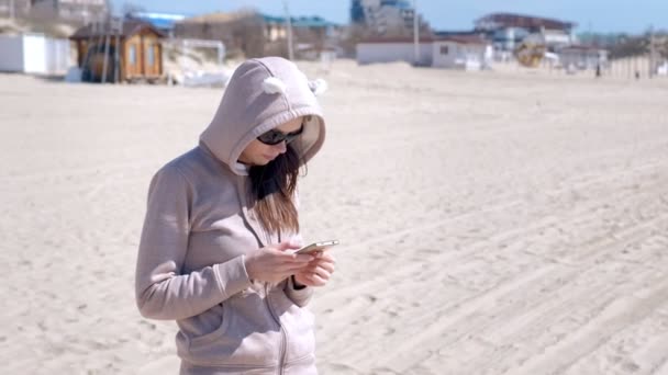 Mujer joven está escribiendo en el teléfono en la playa por mar . — Vídeo de stock