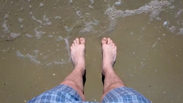 Ο άνθρωπος στέκεται στη θάλασσα γυμνά πόδια στην αμμώδη παραλία. — Αρχείο Βίντεο