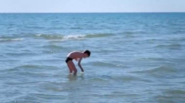 Çocuk Çocuk sahilde ayakta ve oyun ve kabukları arıyor.