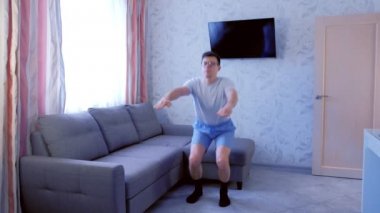 Komik nerd adam oturma odasında evde çömelme ve eller egzersiz yapıyor.