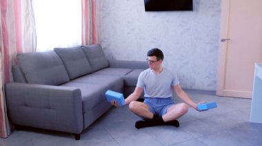Zayıf nerd adam çabaları ile dumbbells yerine yoga blokları ile eller için egzersiz yapıyor. Spor mizah konsepti.