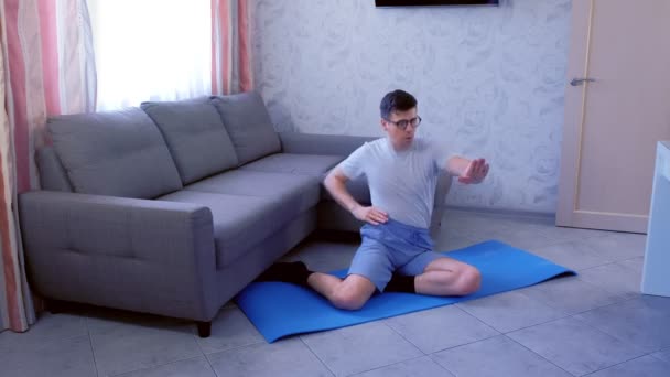 Homem nerd engraçado está fazendo exercícios de moldar as mãos sentado no tapete em casa. Conceito de humor esportivo . — Vídeo de Stock
