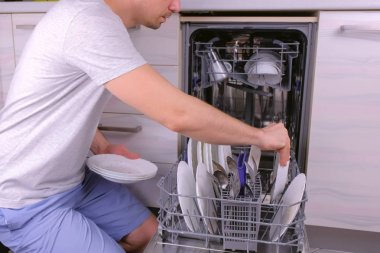 Tanınmayan adam bulaşık makinesine beyaz kirli tabaklar koyup mutfakta çalıştırıyor..