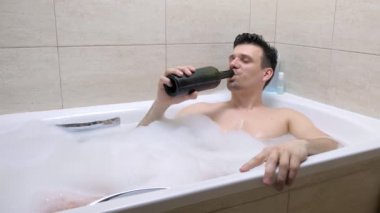 Yorgun 30s adam banyo yatıyor ve kırmızı şarap içecekler.