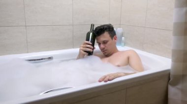 Yetişkin yorgun 30s adam banyoda şişe kırmızı şarap ile uyku.