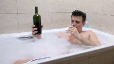 Yorgun sarhoş adam banyoda yatıyor, bir şarap bardağına şarap dökün ve içecek.