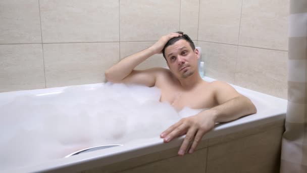 Mann in den 30er Jahren sitzt in Badewanne im Badezimmer und entspannt. — Stockvideo