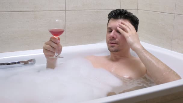 Frustré homme déprimé est couché dans le bain et boire du vin . — Video