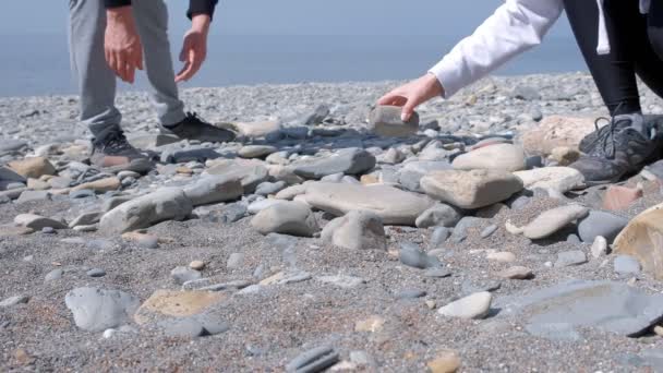 Man and woman are building a brazier of stones on the sea beach, closeup hands. — Stock Video