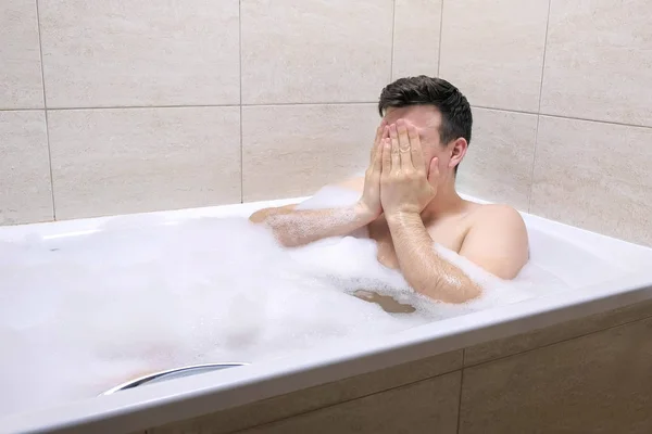 Hombre adulto sentado en el baño en el baño de espuma, limpia la cara con las manos . — Foto de Stock
