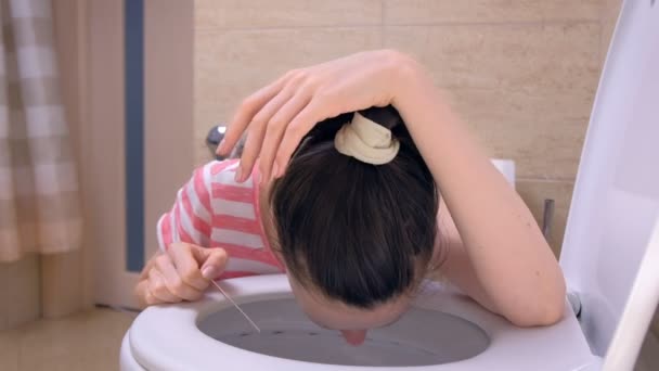 Pregnant young tired woman with pregnancy test in hand is vomiting in toilet sitting on the floor at home. — Stock Video