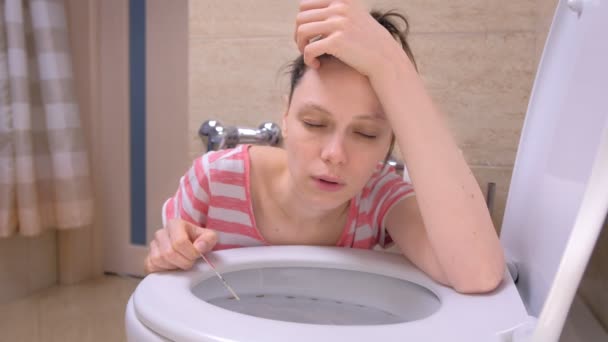 Pregnant tired woman is vomiting in toilet sitting on the floor at home and looking at camera. — Stock Video