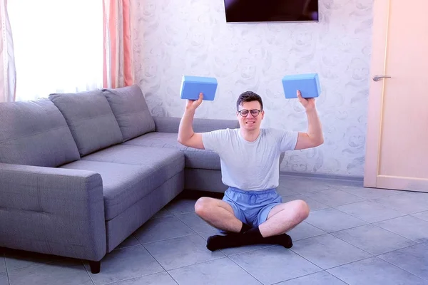 Homem nerd fraco está fazendo exercícios para mãos com blocos de ioga em vez de halteres. Conceito de humor esportivo . — Fotografia de Stock