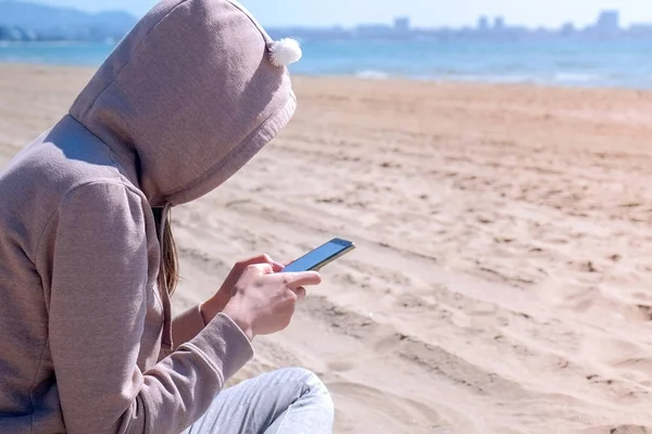 Mulher irreconhecível está digitando no telefone na praia por mar . — Fotografia de Stock
