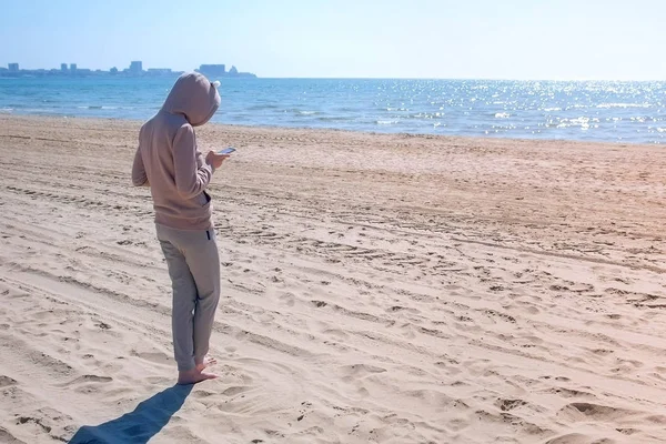 Oigenkännlig kvinna är att skriva på telefon på stranden med havet. — Stockfoto