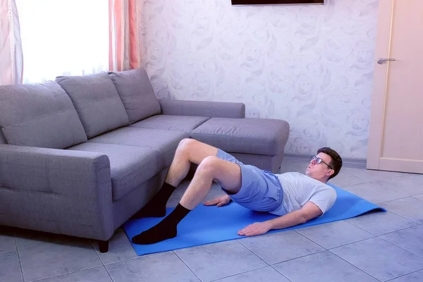Uomo nerd divertente sta facendo esercizio ponte gluteo sul tappeto per rafforzare i muscoli delle gambe a casa. Concetto di umorismo sportivo . — Foto Stock