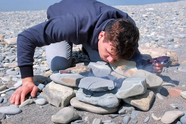 Människan blåste upp kol blåsning på elden på havet stenstrand. Göra Campus brasa. — Stockfoto