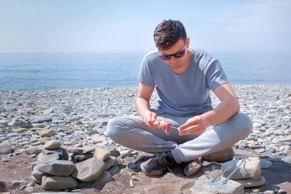 Adam deniz taşı sahilde oturan şiş üzerinde et dilimleri koyarak shashlik hazırlanıyor. — Stok fotoğraf
