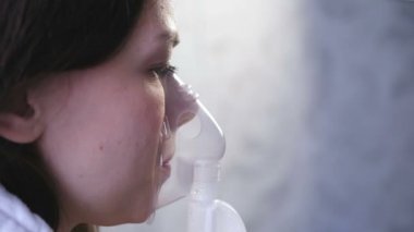 Nebulizatör ve astım tedavisi için kullanın. Genç kadın inhaler maskesi teneffüs edilmesi. Yakın çekim yüz, yan görünüm.