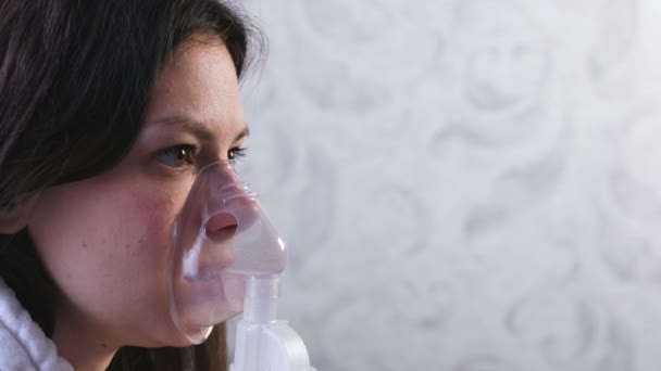 治療のためには、ネブライザーと吸入器を使用します。若い女性は、吸入マスクを通して吸い込むこと。クローズ アップ顔、横から見た図. — ストック動画