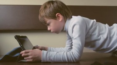 Trendeki çocuk ikinci sınıf bir vagonda tablet oynuyor, yan görünüm.