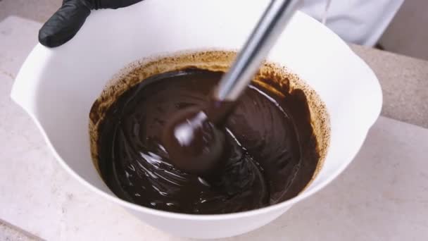 Mix liquid dark chocolate in a white bowl with blender. Close-up view. — Stock Video