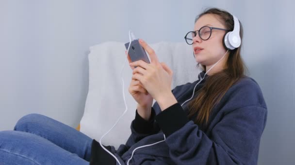 Жінка слухає музику в навушниках на смартфоні і співає пісню. — стокове відео