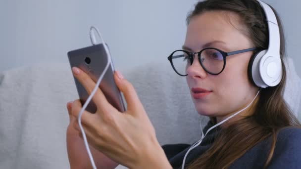 Femme navigue et regarde dans les médias sociaux dans le smartphone en lunettes et écouteurs . — Video