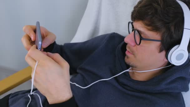 Muž v brýlích a sluchátka hrát hru v smartphone. Gamer relax. — Stock video