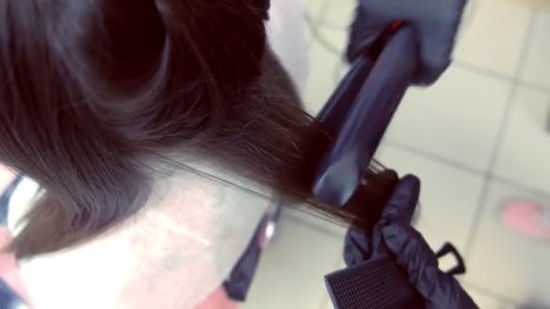 Peluquería alisados cabello castaño oscuro de mujer hermosa usando pinzas para el cabello en el salón de belleza. Primer plano del cabello . — Vídeos de Stock