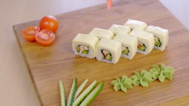 Cook wasabi, marine, kırmızı zencefil ve sebze ile ahşap tahta üstüne tavuk, salatalık, yeşillik ve krem satranç ile rulo hizmet vermektedir.
