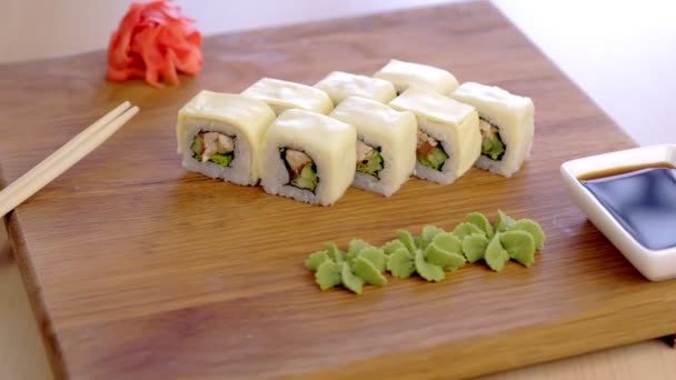 Wasabi, marine, kırmızı zencefil, soya sosu ve sebze ile ahşap tahta üzerinde tavuk, salatalık, yeşillik ve krem satranç ile Rolls. Yan görünüm. — Stok video