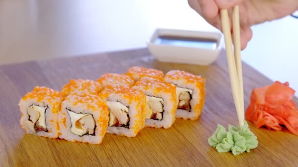 El hombre está comiendo rollos con palos de madera, wasabi, jengibre y salsa de soja. Primer plano de la mano . — Vídeo de stock