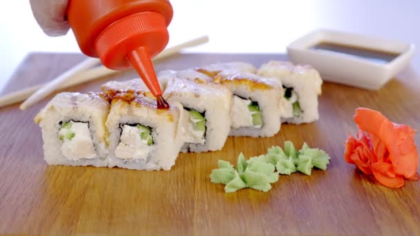 Chef verse des petits pains à la sauce dans une planche de bois avec wasabi, gingembre et saucisse de soja. Gros plan des mains . — Video