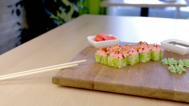 Rollos con caviar verde y salsa en la parte superior sobre tabla de madera con wasabi, jengibre y soja sobre la mesa en la cafetería . — Vídeo de stock