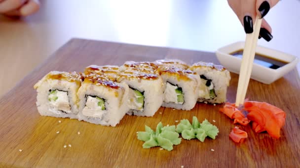 Femme mange des petits pains avec du poisson et des graines de sésame sur le dessus servis en planche de bois avec wasabi, gingembre et saucisse de soja. Gros plan des mains . — Video