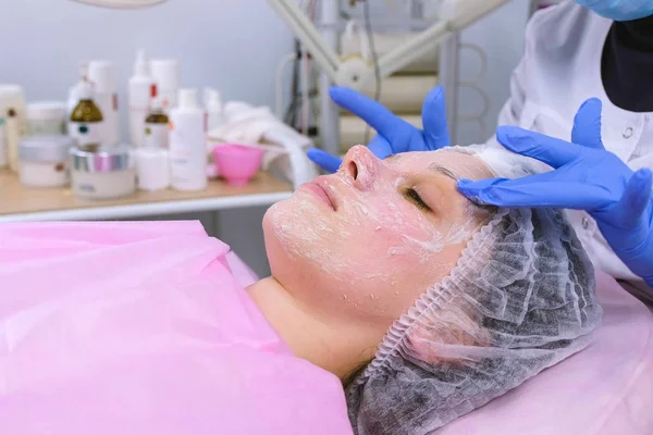 Kosmetolog fjerner og ruller en maske fra kvinders ansigt. Rengøringsansigt. Ansigt close-up . - Stock-foto