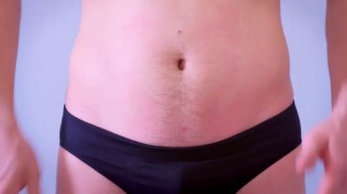Külotlu adam dokunur ve onun sarkık yağ çıplak mide tokatlar, closeup görünümü.
