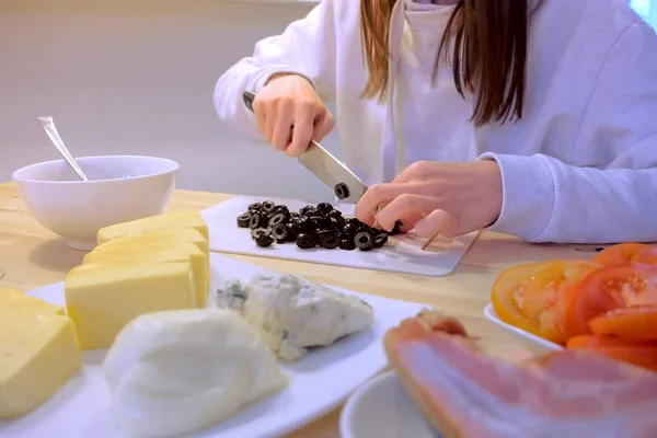 Woman cuts black olives on plastic board, hands close-up.