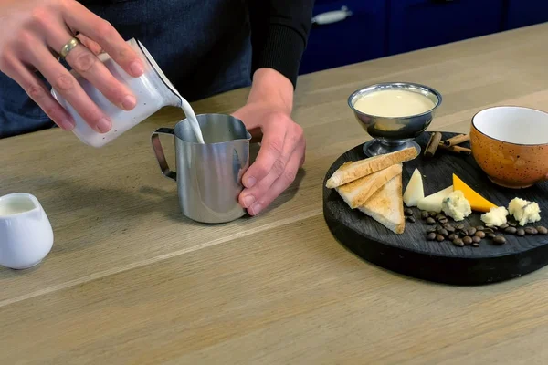 Barista makes cheese coffee, pours milk and cream to pitcher, close-up hands.