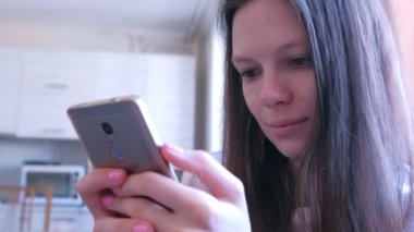 Genç kadın evde mutfakta internet sayfalarında tarama akıllı telefon okuyor.