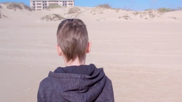 Enfant garçon marche sur la plage de sable aux dunes de sable vue arrière activités de plein air . — Video