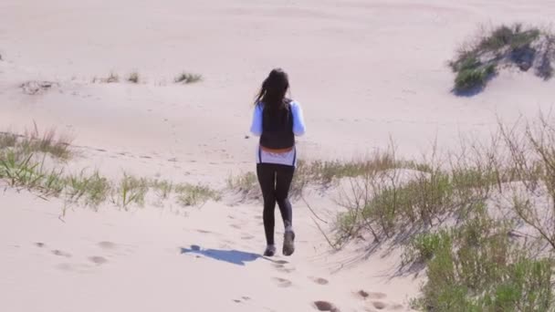С песчаной дюны спускается женщина-путешественница с рюкзаком. . — стоковое видео