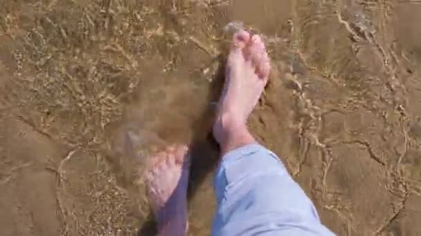 Homem está andando na água rasa na areia pernas inferiores fechar as férias de verão . — Vídeo de Stock