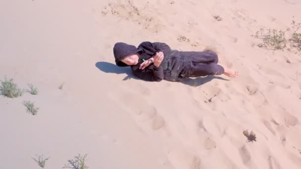 Menino está jogando rolando pelas dunas de areia na praia de férias . — Vídeo de Stock