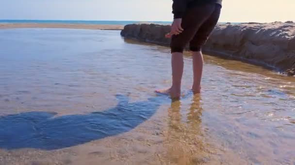 Kind jongen loopt op ondiep water in de rivier stroomt in de zee blote voeten benen. — Stockvideo