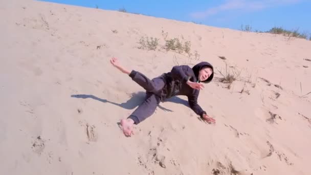 Niño feliz está rodando y cayendo por la playa de dunas de arena en vacaciones . — Vídeo de stock